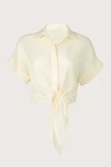 Camisa crop fluida de manga corta color crema con cuello camisero, botonadura frontal oculta y detalle de nudo en el frente.