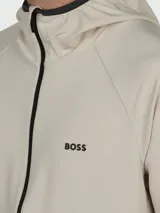 Campera técnica con capucha de la marca Boss, en color beige claro. Presenta cierre frontal completo en contraste negro, mangas largas con terminaciones elásticas y logo de la marca estampado en el pecho.