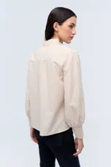 Camisa color crema a rayas verticales con bordado floral en el pecho, cuello mao y mangas largas abullonadas con puños elásticos.