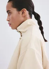 Chaqueta de algodón estilo denim, de diseño oversize, color beige, con cuello alto, manga larga, bolsillos de parche con solapa y cierre frontal de botones oscuros.