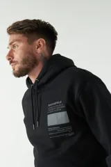 Buzo canguro negro con capucha ajustable y bolsillo frontal. Presenta un estampado gráfico en el pecho con texto y líneas decorativas, además de un detalle estampado en la manga.