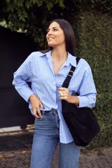 Bolso negro de cuero gamuzado con correa larga regulable y logo de la marca grabado en el frente.