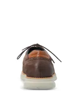 Zapato de estilo casual con cordones, confeccionado en cuero marrón con detalles de perforaciones decorativas tipo brogue. Cuenta con una suela de EVA flexible y ligera en color gris claro con un pequeño detalle naranja en el lateral.
