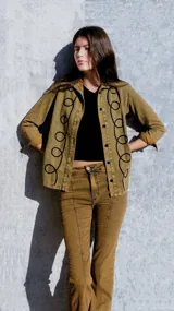 Camisa de denim color marrón con bordados negros en el frente, de corte recto y mangas largas.