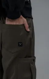 Pantalón cargo de corte regular confeccionado en textil técnico pesado color chocolate. Presenta cintura elástica con cordón de ajuste, dos bolsillos laterales en la cintura y dos bolsillos cargo de gran tamaño. Incluye elásticos con tancas en los tobillos para regular la apertura de la pierna.