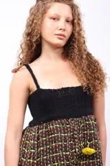 Top de diseño artesanal con cuerpo superior tejido en crochet negro y parte inferior de corte peplum en tejido plano de telar con trama a cuadros en tonos oscuros, rojo y amarillo.