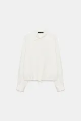 Camisa de satén con cuello solapa, manga larga con puños y bajo ajustable mediante cordones. Presenta cierre frontal con botones ocultos.