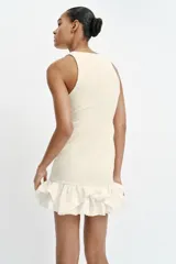 Vestido corto de color blanco con cuello redondo y diseño sin mangas. Presenta un cuerpo de tejido bouclé texturizado y un bajo acabado con volantes de tejido ligero.