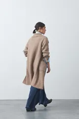 Cardigan de tejido de punto gris, con silueta larga, frente abierto, solapas clásicas y bolsillos aplicados en los laterales.