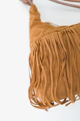 Cartera tipo bandolera color rojo oscuro, con flecos en la parte inferior y cierre de cremallera. Tiene una correa fina con un nudo decorativo.