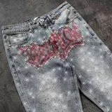 Pantalón de jean con corte recto y acabado desgastado, decorado con pedrería brillante en toda la superficie y un diseño de graffiti en color rojo con cristales en la zona frontal.
