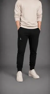 Pantalón tipo jogger de corte ajustado, color negro, con cintura elástica y puños acanalados en los tobillos. Presenta un pequeño logo bordado en color claro en el muslo derecho.