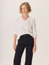 Remera blanca de manga tres cuartos con cuello en V y sutil estampado en el centro del pecho. Las mangas terminan con un detalle de volado elástico.
