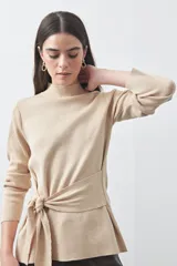 Polera de tejido de punto color beige, con cuello alto, manga larga y detalle de lazo ajustable en la cintura que aporta estructura a la silueta.