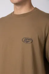 Remera de manga larga con diseño de doble capa, que simula una remera de manga corta color moka sobre una de manga larga blanca. Presenta un pequeño logo gráfico en el pecho y un detalle de etiqueta en el puño.