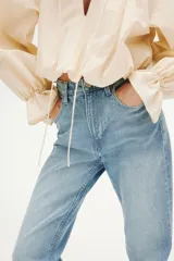 Pantalón jean de tiro alto y corte bootcut, confeccionado en denim de algodón con ligera elasticidad. Presenta diseño clásico de cinco bolsillos, cierre frontal con botón y cremallera, y perneras ligeramente acampanadas en el bajo.