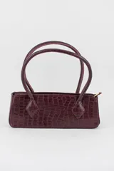 Cartera tipo baguette color negro con textura efecto cocodrilo, diseño alargado, doble asa de mano y cierre superior.
