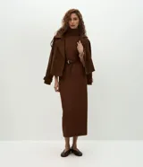 Vestido midi de color marrón, confeccionado en tejido de poliéster con elastano. Presenta un diseño ajustado al cuerpo, cuello alto, mangas 3/4 y una abertura trasera en el bajo para mayor movilidad. Incluye un cinturón fino del mismo tono.
