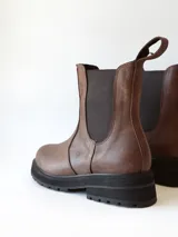 Bota tipo Chelsea de cuero color chocolate, con paneles elásticos laterales, tirador trasero y suela track negra de goma.