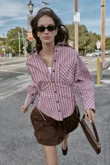 Camisa de manga larga con estampado de cuadros en tonos rosados y negros. Presenta cuello solapa, bolsillo delantero de plastrón, cierre frontal con botones y detalle de laterales ajustables con lazos.