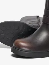 Botas de media caña de cuero sintético en color marrón oscuro con efecto avejentado, tacón ancho y suela flatform. Cuentan con cierre lateral interno y tiras decorativas con hebilla metálica y argolla en el tobillo.