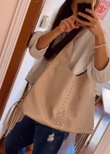 Cartera estilo hobo de cuero sintético color beige, con flecos laterales, detalle de tachas metálicas verticales en el frente y aplique con estrellas grabadas en la base.