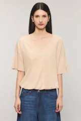 Remera oversize color beige, con escote en V, mangas cortas y cintura con elástico efecto balloon. Confeccionada en jersey Pima flamé de algodón, con bordado marcario en la manga.