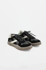 Zapatillas urbanas de cuero con paneles en gamuza negra y detalles en cuero color crema. Presentan suela de goma texturizada en tono marrón y cordones bicolores.