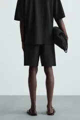 Bermuda de hombre color verde claro, de corte regular y tiro medio, con pinzas frontales, bolsillos laterales y bolsillos traseros de vivo. Cierre frontal con botón y cremallera.