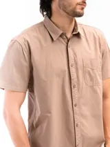 Camisa de manga corta color celeste claro, confeccionada en algodón, con cuello clásico y un bolsillo de parche en el lado izquierdo del pecho.