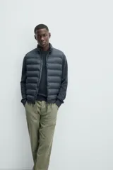 Chaleco acolchado verde oscuro, con cuello alto, cierre frontal con cremallera y bolsillos laterales. Confeccionado en tejido técnico repelente al agua.