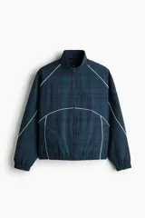Campera deportiva de nylon en color verde oscuro con estampado a cuadros, cuello elevado, cierre frontal y ribetes blancos en contraste. Cuenta con elástico en puños y bajo, y forro de malla.