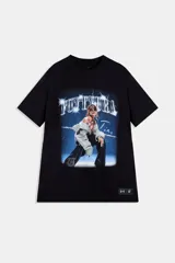 Remera negra de algodón con cuello redondo y mangas cortas, perteneciente a la colaboración Tini x Under Armour. Presenta un estampado gráfico frontal de estilo Y2K con la inscripción 'FUTTTURA' y la imagen de la artista Tini, además de una etiqueta deportiva en el dobladillo inferior derecho.