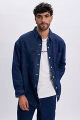 Sobrecamisa de jean color azul oscuro, de corte oversize, con mangas largas, bolsillos frontales con solapa y cierre con broches a presión.