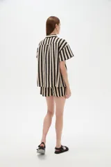 Camisa de algodón de corte holgado, con diseño de rayas verticales en colores negro y beige, cuello camisero y cierre frontal con botones.