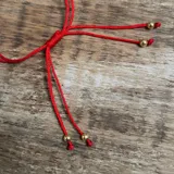 Pulsera de hilo con dije circular de circnia con baño en oro y cierre regulable.