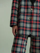 Pantalón de tiro alto con corte ancho y recto, confeccionado en tela de algodón con estampado de cuadros escoceses en tonos azul marino, verde y rojo. Presenta cierre frontal oculto con botones internos y pasacintos en la cintura.