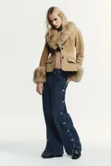 Pantalón de jean azul oscuro, de corte amplio y tiro medio, con bolsillos delanteros y traseros. Presenta una hilera de botones metálicos a lo largo de cada lateral.