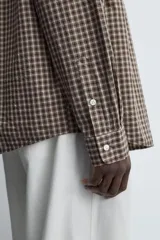 Camisa relaxed fit de algodón con estampado de cuadros en tonos marrón y beige. Cuenta con cuello solapa, manga larga con puño abotonado, bolsillo plastrón en el pecho y cierre frontal de botonadura.
