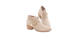 Bota corta de cuero gamuzado color avena, con taco fachetado efecto madera de 5 cm, punta redondeada y detalle de hebilla dorada lateral.