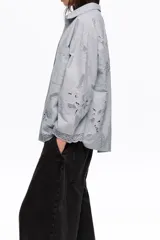 Camisa de manga larga color celeste, de corte holgado, con cuello clásico, cierre frontal de botones, bolsillo en el pecho y detalles de bordados florales y encaje en el ruedo y los puños.
