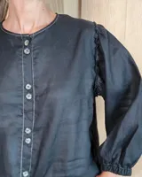 Camisa de manga larga con diseño de rayas verticales y bordados sutiles. Presenta cuello redondo, cierre frontal con botones y mangas abullonadas con volados en los hombros.