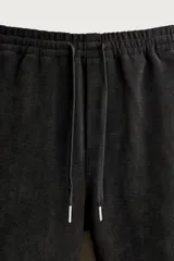 Pantalón jogger de corte relajado en color negro, confeccionado en tejido con elasticidad. Presenta cintura elástica con cordón ajustable y bolsillos laterales decorados con tachas metálicas.