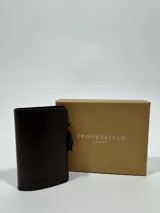 Billetera tarjetero marrón de cuero sintético con logo de la marca grabado en el frente.