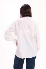 Camisa blanca de corte oversize con textura de rayas verticales sutiles. Presenta cuello mao, cierre frontal con botones y mangas largas abullonadas con puños anchos.