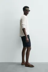 Camiseta de algodón color beige claro, de corte relajado (relaxed fit) con cuello redondo y manga corta. Presenta una textura sutil en el tejido.