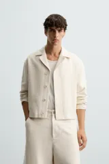 Sobrecamisa de hombre color crema, confeccionada en tejido con estructura, de corte regular fit. Presenta cuello bowling, manga larga y bolsillos delanteros ocultos en costura. Cierre frontal con botonadura oculta por solapa.