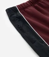 Pantalón de jogging color bordó con paneles laterales en negro y detalles de líneas blancas. Presenta un corte holgado y cintura elástica con cordón de ajuste.