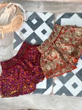 Short de seda con elástico fruncido en la cintura y volado en el ruedo. Presenta un estampado vibrante en tonos rojo/bordó y turquesa con motivos florales o arabescos.