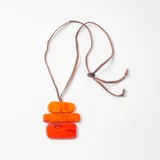 Collar con dije compuesto por tres piezas rectangulares de resina en degradado de tonos naranjas y rojos, suspendido de un cordón de cuero ajustable.